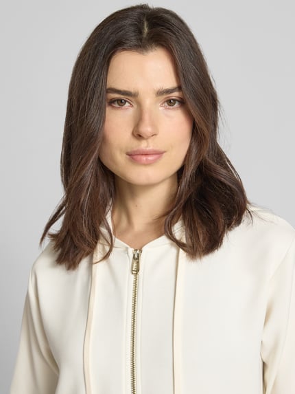 Frauenmodel trägt Sweatjacke mit Halbarm Modell 'Therese' von JOOP! in Creme, Elastischer-Material-Mix, Reißverschluss, Label-Detail, Nahaufnahme Oberkörper.