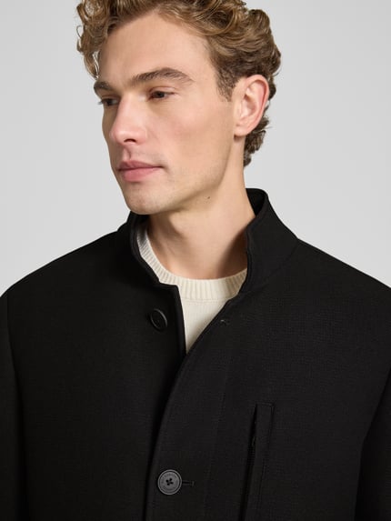Männermodel trägt Regular Fit Mantel mit Knopf- und Reißverschluss von ROY ROBSON in Schwarz, strukturierte Oberfläche, Nahaufnahme Oberkörper.