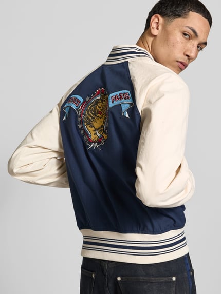 Männermodel trägt Regular Fit Collegejacke aus reiner Baumwolle von Kenzo, dunkelblau-cremefarben, Label-Stitching, Rückenansicht, Nahaufnahme Oberkörper. Reine Baumwolle, durchgehende Knopfleiste, Eingrifftaschen, Stickerei, Rückenlänge 60 cm, Schulterbreite 45 cm, Ärmellänge 64 cm.