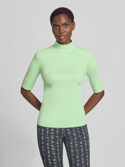Modelka nosi Slim Fit T-Shirt aus Baumwoll-Mix mit Stehkragen von Marc Cain, damski t-shirt w kroju slim fit z mieszanki bawełny, stójka, rękaw o dł. 1/2, długość tyłu w rozmiarze 36: 54 cm, jasny zielony kolor, gładka faktura, widok całej sylwetki z przodu.
