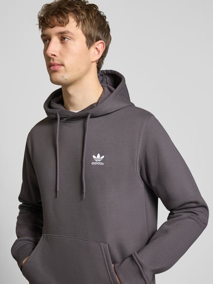 Männermodel trägt Regular Fit Hoodie aus Baumwoll-Mix von adidas Originals in Uni-Grau mit Logo-Stitching, Nahaufnahme Oberkörper.