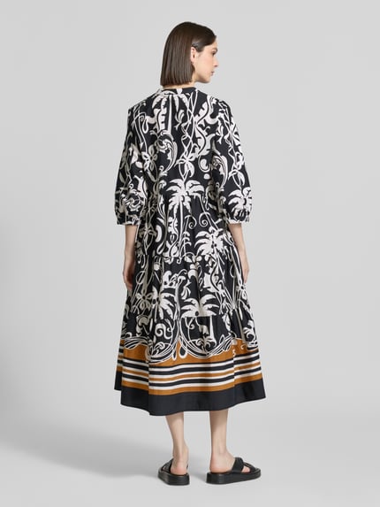 Vrouwenmodel draagt Midikleid met Eingrifftaschen und 3/4-Arm van Emily Van den Bergh, zwart-wit alloverprint, a-lijn, rugaanzicht, katoen.
