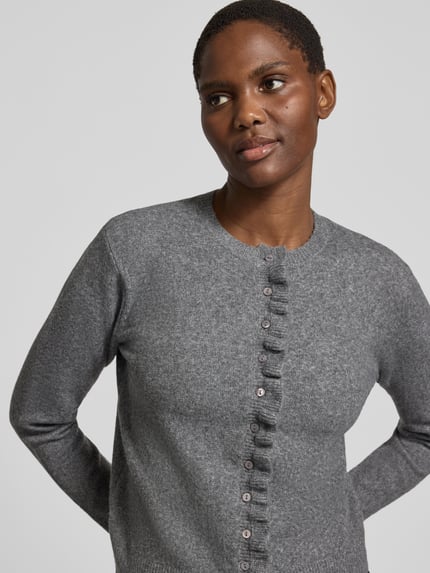 Modelka kobieca ma na sobie Regular Fit Strickjacke aus elastischem Baumwoll-Mix von zero, mieszanka bawełny i elastanu, krój regular fit, listwa guzikowa, obszycie falbanami, długość tyłu w rozmiarze 36: 52 cm, długość rękawów w rozmiarze 36: 60 cm, odcień szarości, gładka dzianina, widoczna tekstura, jednolite guziki, zdjęcie z przodu, ujęcie zbliżone na górną część ciała.