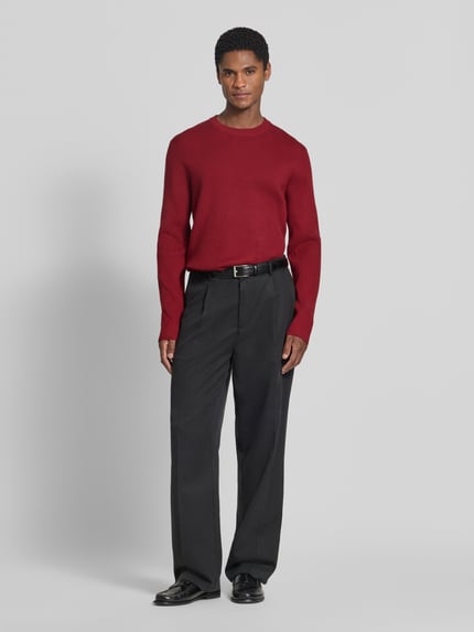 Männermodel trägt Slim Fit Strickpullover Baumwoll-Mix von Lindbergh in Rot, gerippte Optik, Rundhalsausschnitt, Ganzkörperansicht von vorne.