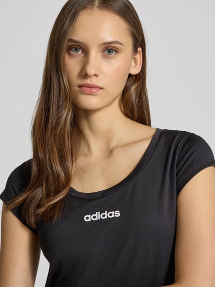 Frauenmodel trägt Cropped T-Shirt mit Label-Print von adidas Sportswear aus Material-Mix mit Stretch-Anteil, Schwarz, Nahaufnahme Oberkörper.