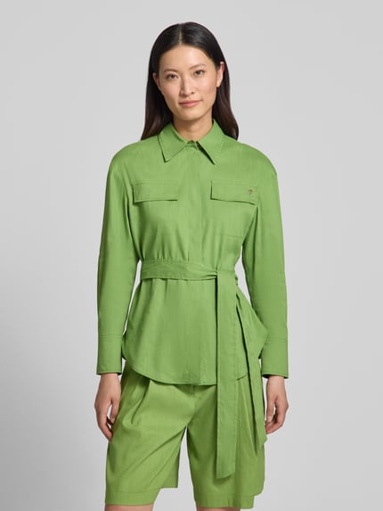 Frauenmodel trägt Bluse aus Leinen-Mix mit Brusttaschen von Marc Cain in Grün, taillierte Passform, Stoffband, Umlegekragen, Nahaufnahme Oberkörper. Rückenlänge bei Größe 36: 69 cm, Ärmellänge bei Größe 36: 55 cm, Leinen-Viskose-Anteil.