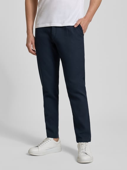 Mężczyznamodel nosi Tapered Fit Chino aus Baumwoll-Mix Modell 'CHINO PLEATED' od BOSS Orange, granatowy twill, gładka faktura, boczne kieszenie, krój tapered fit, widok całej sylwetki z przodu.