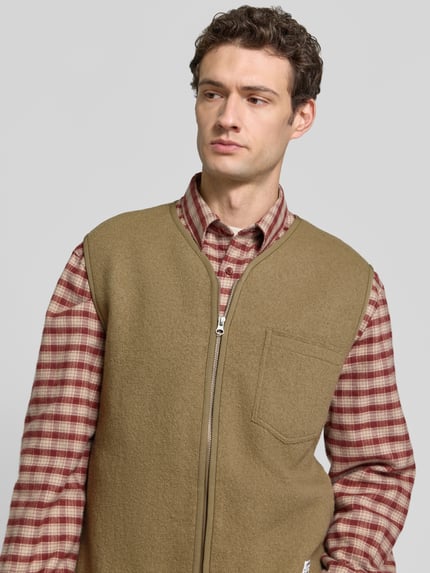 Männermodel trägt Weste aus Wolle mit Zweiwege-Reißverschluss Modell 'HANNES' von Samsøe Samsøe in Beige, Nahaufnahme Oberkörper. Reine Wolle, Regular Fit, V-Ausschnitt, Brusttasche, Label-Detail, Rückenlänge 68 cm, Schulterbreite 47 cm, Brustweite 57 cm.