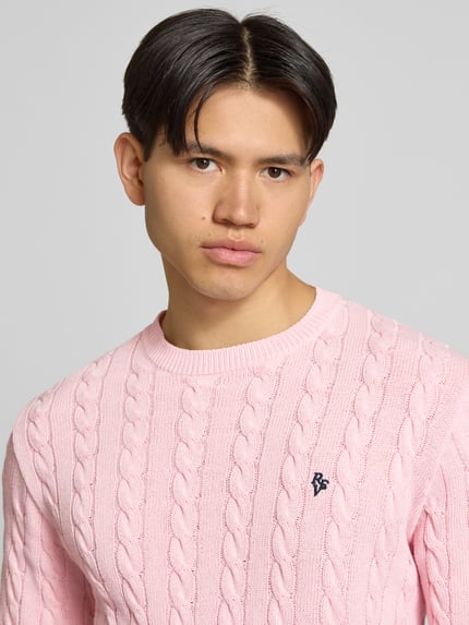 Männermodel trägt Strickpullover mit Zopfmuster und Logo-Stitching von REVIEW aus Baumwoll-Mix in Rosa, Nahaufnahme Oberkörper.