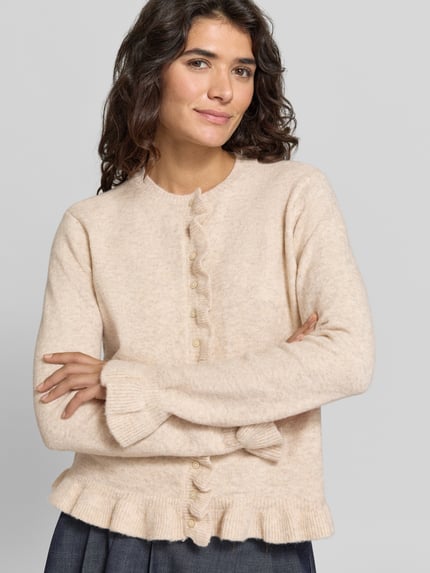 Frauenmodel trägt Regular Fit Cardigan mit Rundhalsausschnitt Modell 'Jacia' von VILA, cremefarben, Rüschen, Knopfleiste, Material-Mix mit Woll-Anteil, Nahaufnahme Oberkörper.