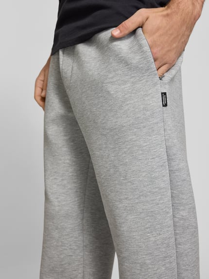 Männermodel trägt Regular Fit Sweatpants aus Material-Mix Modell 'BILL LEGACY' von JACK & JONES in Hellgrau, Eingrifftaschen, Nahaufnahme Oberschenkel, Herren Sweatpants, elastischer Bund mit Tunnelzug, Innenbeinlänge bei Größe M 77 cm.