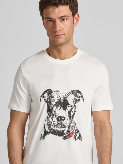 Männermodel trägt Regular Fit T-Shirt aus reiner Baumwolle Modell 'DUBROX' von HUGO, unifarben, Motiv-Print, Nahaufnahme Oberkörper.