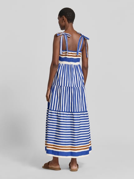 Frauenmodel trägt Midikleid im Stufen-Look von Stefanel aus Reine Baumwolle mit A-Linie und Karree-Ausschnitt, gestreiftes Muster, Ganzkörperansicht Rückansicht.