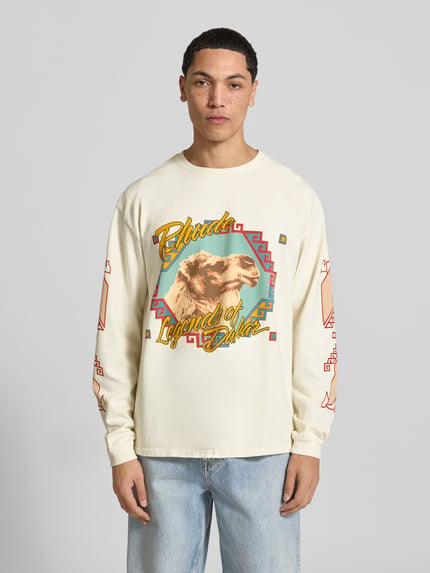 Männermodel trägt Relaxed Fit Longsleeve aus puur katoen van RHUDE met labelprint, ronde hals en elastische mouwboord, ruglengte maat M 70 cm, Ganzkörperansicht von vorne.