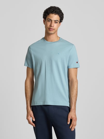 Männermodel trägt T-shirt met labelstitchings en ronde hals van CHAMPION in lichtblauw, puur katoen, regular fit, ruglengte maat M 66 cm, Ganzkörperansicht van voren.