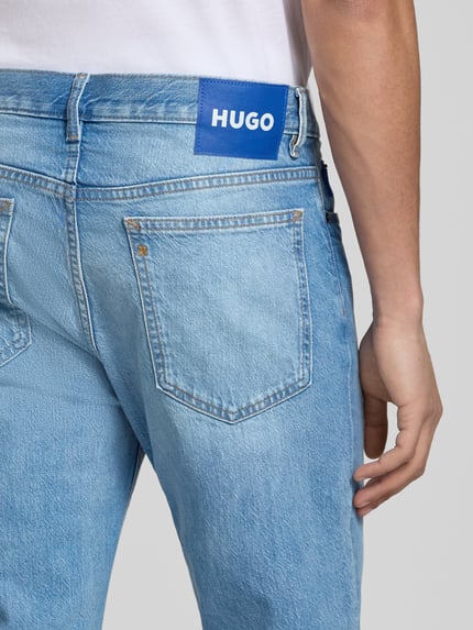 Mężczyznamodel nosi Straight Fit Jeans aus Baumwolle od HUGO, efekt: jednolity kolor, krój straight fit, detal z logo, 5 kieszeni, zapięcie na guzik i zamek błyskawiczny, średni stan, bawełna. Detailaufnahme.