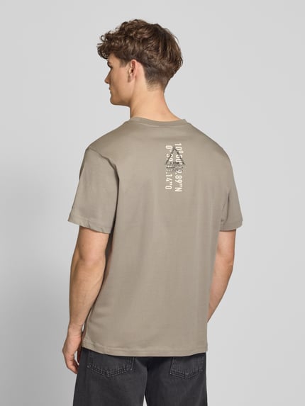 Männermodel trägt T-Shirt aus Baumwolle mit Rundhalsausschnitt von G-Star Raw in Beige, Regular Fit, glatte Textur, Rückendruck, Ganzkörperansicht Rückansicht.