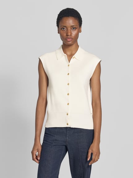 Frauenmodel trägt Relaxed Fit Weste aus Baumwoll-Mix von Tommy Hilfiger in Creme mit goldfarbenen Knöpfen, kombiniert mit Jeans, Ganzkörperansicht von vorne. Damen Weste von Tommy Hilfiger.