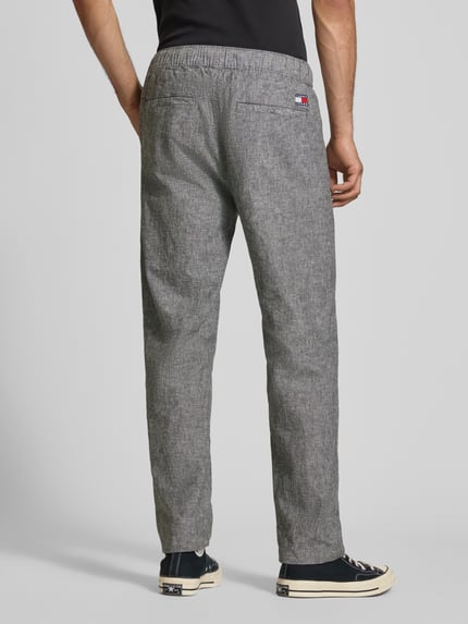 Männermodel trägt Regular Fit Weite HOSE aus Leinen-Baumwoll-Mix von Tommy Jeans in Melange-Optik mit Label-Stitching und elastischem Bund, Ganzkörperansicht Rückansicht.