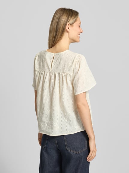 Frauenmodel trägt Blusenshirt mit Stitchings Modell 'LANA' von ICHI aus Baumwoll-Viskose-Mix in Creme, Regular-Fit, Rückenlänge 54 cm, Kurzarm, Ganzkörperansicht Rückansicht.