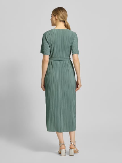 Modelka prezentuje sukienkę koktajlową w kopertowym stylu model 'LINDA' od YAS, taliowany krój, sukienka midi, wiązany pasek, dekolt w serek, wydłużony tył, długość tyłu w rozmiarze 36: 129 cm, szerokość w rozmiarze 36: 43 cm, długość rękawów w rozmiarze 36: 26 cm, jednolity zielony kolor, plisowana tekstura, widok całej sylwetki z tyłu.