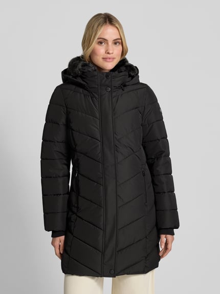 Frauenmodel trägt Jacke mit abnehmbarer Kapuze von NAUTGÅRD in Schwarz mit gestepptem Design, Reiß- und Druckknopfverschluss, Ganzkörperansicht von vorne. Rückenlänge 85 cm, Schulterbreite 43 cm, Brustweite 48 cm, Ärmellänge 48 cm, gestrickte Ärmelabschlüsse, Label-Patch, seitliche Reißverschlusstaschen.
