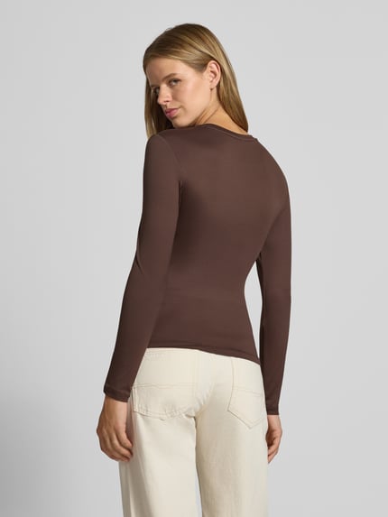 Frauenmodel trägt Slim Fit Langarmshirt mit Rundhals-Ausschnitt Modell 'LULA' von PIECES in Braun zu heller Hose, Ganzkörperansicht Rückansicht. Damen Langarmshirt von PIECES.
