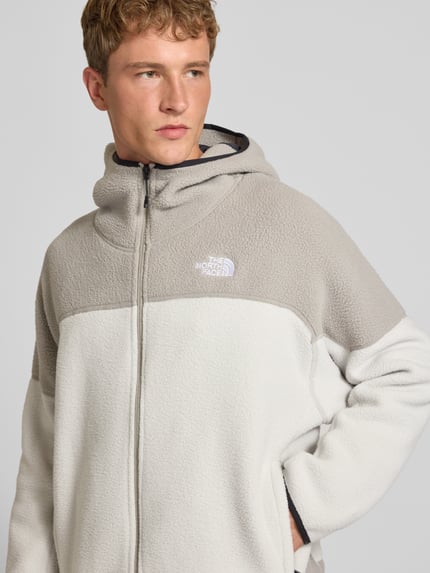 Männermodel trägt Fleecejacke mit Kapuze und Logo-Stitching von The North Face in Creme und Hellgrau, Nahaufnahme Oberkörper, Herren Fleecejacke, Regular Fit, Reißverschluss, Seitentaschen, KI-modifiziertes Bild
