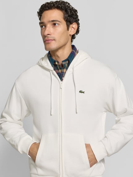 Męski model nosi Regular Fit Sweatjacke aus Baumwoll-Mix von Lacoste, Herren Sweatjacke, kremowy kolor, gładka faktura, zbliżenie górnej części ciała