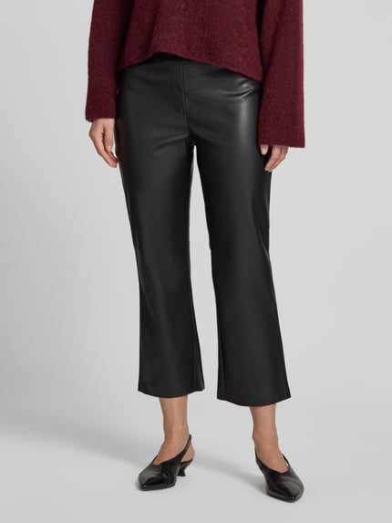Frauenmodel trägt Flared Fit Hose in -Optik von Christian Berg Woman, schwarze Farbe, glatte Textur, elastischer Bund, verkürzte Passform, Ganzkörperansicht von vorne. Kontext: Damen Hose, Bundweite 38 cm, Innenbeinlänge 64 cm.