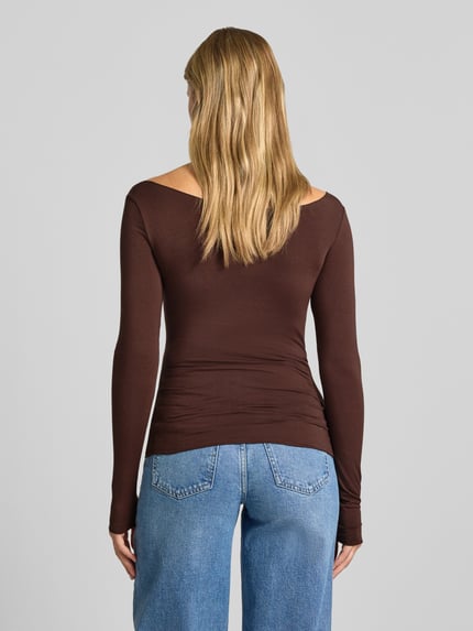 Frauenmodel trägt Slim Fit Langarmshirt U-Boot-Ausschnitt von REVIEW in Braun, glatte Struktur, kombiniert mit Jeans, Ganzkörperansicht Rückansicht. Lyocell-Mix mit Stretch-Anteil, elastischer Bund, Rückenlänge Größe S 51 cm.