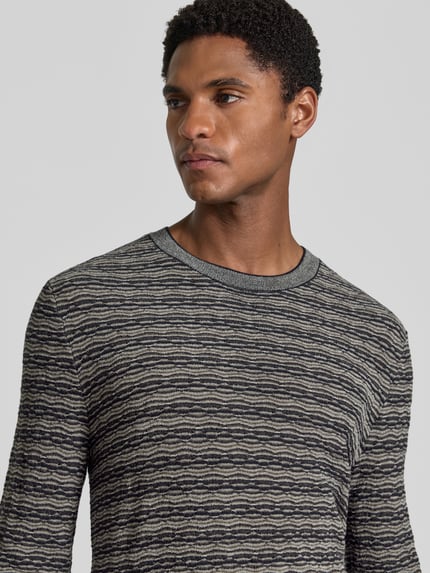 Männermodel trägt Strickpullover mit Lanawolle von Emporio Armani, grau gemustert, Rundhalsausschnitt, Nahaufnahme Oberkörper.