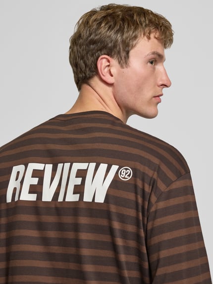 Männermodel trägt Gestreiftes Langarmshirt mit Logoprint vorne und hinten von REVIEW, braun mit weißen Streifen, Reine Baumwolle, Regular Fit, Rundhalsausschnitt, Logoprint am Rücken, Ganzkörperansicht Rückansicht.