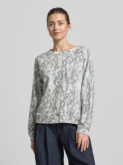 Frauenmodel trägt Comfort Fit Sweatshirt aus Baumwoll-Mix von Tom Tailor Denim mit abstraktem Allover-Muster, Rundhals, Raglanärmel, Logo-Applikation, helle Grau- und Blautöne, weiche Struktur, Ganzkörperansicht von vorne.