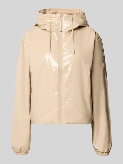 Produktfoto, glänzende beige Jacke mit Kapuze Modell 'Lohja' von RAINS, Reißverschluss, Tunnelzug, Label-Detail auf glatter Oberfläche