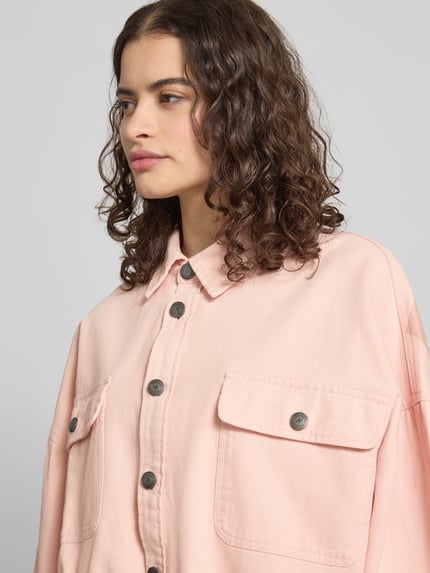 Frauenmodel trägt Oversized Hemdjacke mit Brusttaschen von Karo Kauer aus reiner Baumwolle in Rosa, Umlegekragen, Knopfleiste, Nahaufnahme Oberkörper.