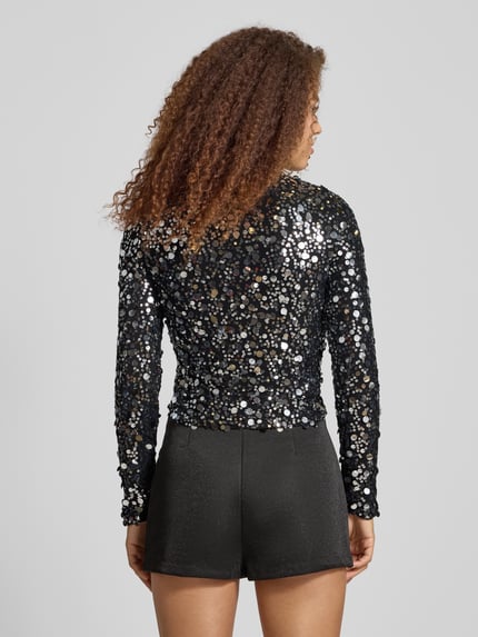 Frauenmodel trägt Slim Fit Langarmshirt mit Paillettenbesatz Modell 'CATINA' von Only, schwarz, glänzende Mesh-Optik, Ganzkörperansicht Rückansicht.