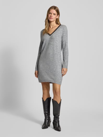 Frauenmodel trägt tailliertes, melangefarbenes Strickkleid mit V-Ausschnitt und Spitzenbesatz, Modell 'TAMMY' von Only, Ganzkörperansicht von vorne.