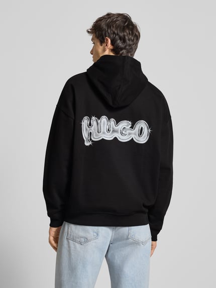 Männermodel trägt schwarzen Relaxed Fit Hoodie aus reiner Baumwolle Modell 'NYROHOOD' von Hugo Blue mit Label Print, Ganzkörperansicht Rückansicht.