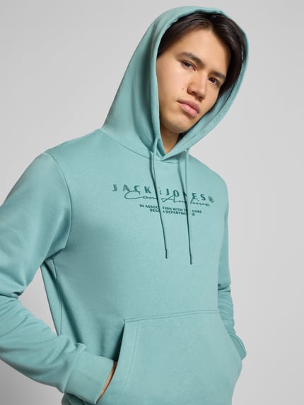 Männermodel trägt Hoodie mit Label-Print von Jack & Jones in Hellblau, Baumwoll-Mix, lockerer Schnitt, Nahaufnahme Oberkörper.