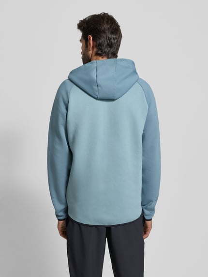 Męski model nosi Kurtka treningowa z zamkiem błyskawicznym dwustronnym Model 'Unstoppable' od Under Armour, mieszanka bawełny, krój regular fit, kaptur, długość tyłu 71 cm, długość rękawów 60 cm, kolor jasnoniebieski, gładka tekstura, widok całej sylwetki z tyłu.