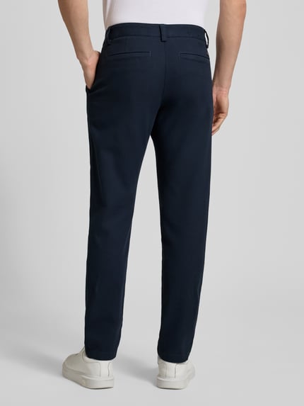 Mężczyzna nosi Tapered Fit Chino aus Baumwoll-Mix Modell 'CHINO PLEATED' od BOSS Orange, granatowa tkanina twill, widoczne kieszenie tylne i pasek, gładka faktura, ganzkörperansicht rückansicht.