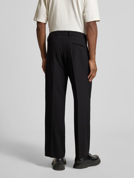 Männermodel trägt Wide Fit Hose mit Bügelfalten Modell 'Leek' von Drykorn, schwarzer Material-Mix mit Viskose-Anteil, Ganzkörperansicht Rückansicht. Bundweite 42 cm, Innenbeinlänge 72 cm, Größe 32/32.