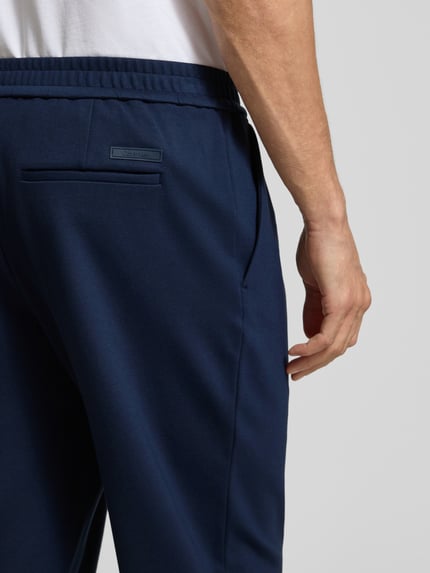 Männermodel trägt Stoffhose mit elastischem Bund von CK Calvin Klein, dunkelblau, Baumwoll-Elasthan-Mix, Gesäßtasche, Detailaufnahme Rückansicht.