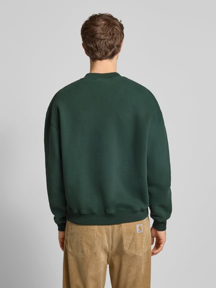 Männermodel trägt Sweatshirt mit Logo und Rundhalsausschnitt von BLKVIS in Dunkelgrün aus reiner Baumwolle im Relaxed-Fit, Ganzkörperansicht Rückansicht. Rückenlänge bei Größe M 66 cm, Ärmellänge 61 cm.