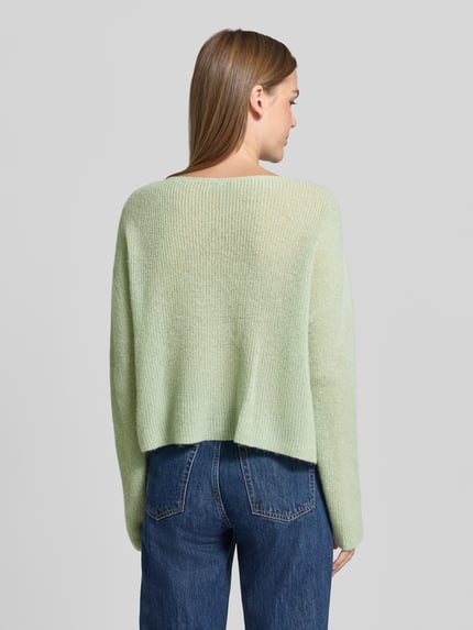 Vrouwenmodel draagt Oversized Wollpullover aus Alpaka-Mix van DRYKORN in lichtgroen, riblook, rechte vorm, Ganzkörperansicht rugaanzicht, Ruglengte maat S: 48 cm, Mouwlengte maat S: 70 cm, Mix van alpaca en wol