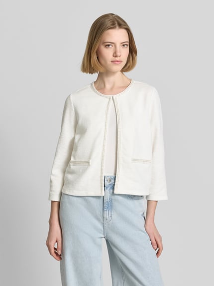 Modelka nosi Regular Fit Jacke mit Zierbordüre von More & More, biały kolor, bawełniany materiał, faktura lekko ziarnista, przód z otwartym designem, kobieca kurtka, długość tyłu 48 cm, długość rękawa 47 cm, krój regular fit, widok całej sylwetki z przodu.