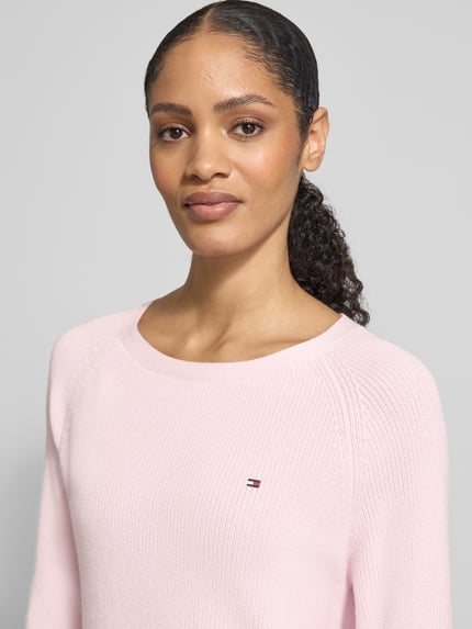 Frauenmodel trägt Regular Fit Pullover aus reiner Baumwolle von Tommy Hilfiger in Rosa mit Rundhals, Logo-Stitching, Rippstrick, Nahaufnahme Oberkörper.