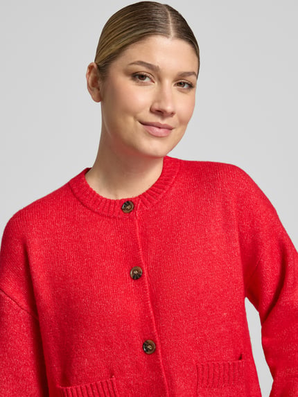 Frauenmodel trägt Cardigan mit aufgesetzten Taschen von Christian Berg Woman in leuchtendem Rot, Feinstrickstruktur, Nahaufnahme Oberkörper.