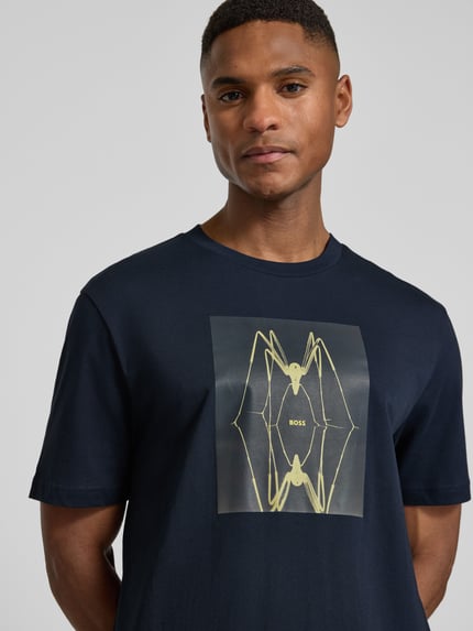 Mężczyznamodel nosi Regular Fit T-Shirt aus reiner Baumwolle Modell 'TE_CREATURE' von BOSS Orange, ciemnogranatowy jersey z motywem, nahaufnahme górnej części ciała.
